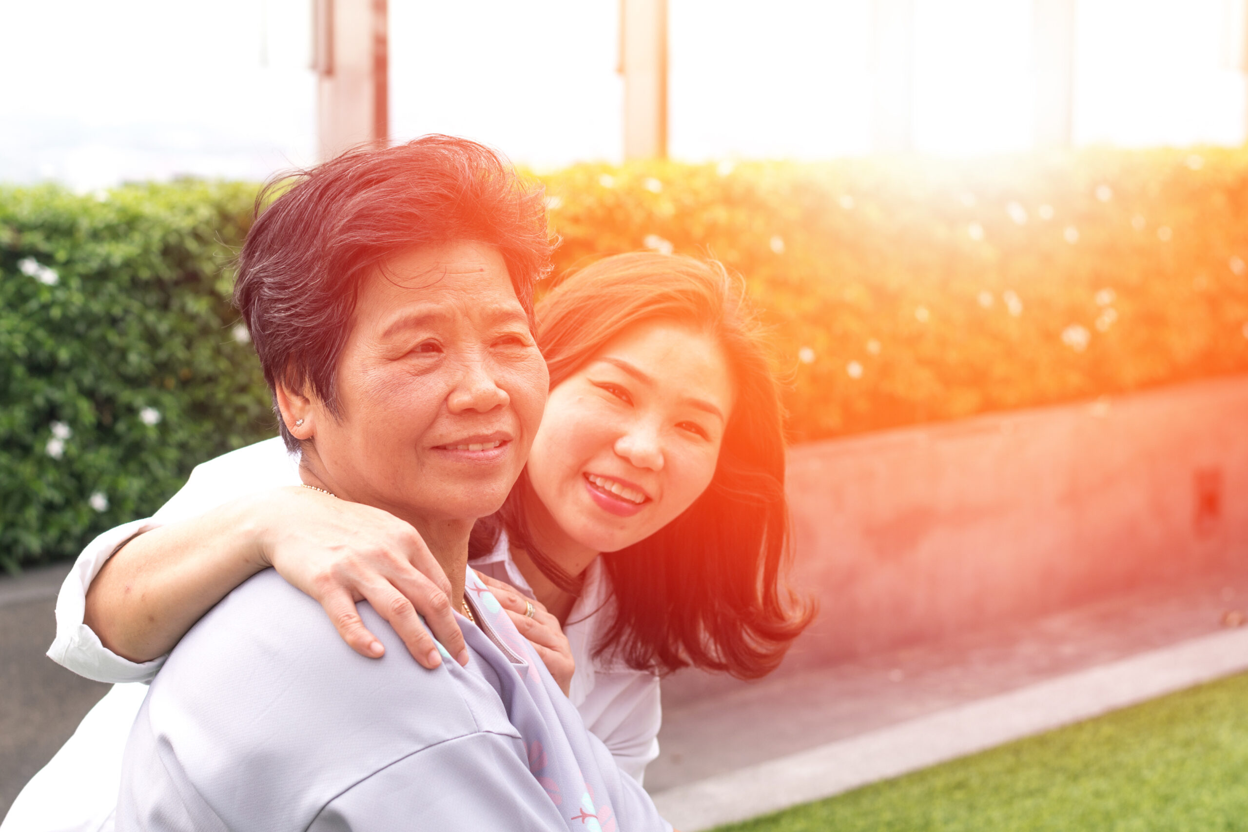 Pretty, young Asian woman with her arms around an older Asian woman outdoors during sunset